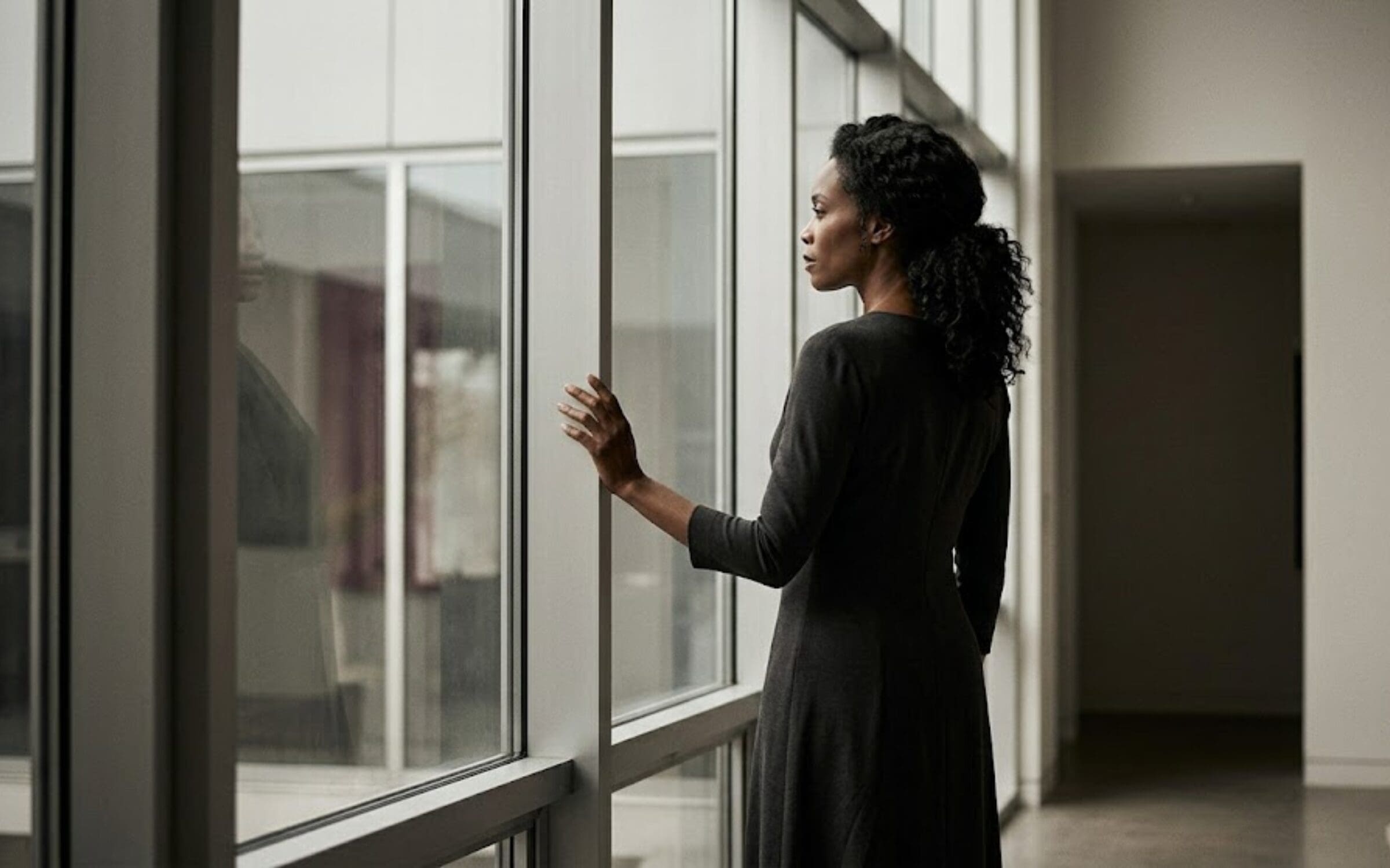 Professional woman standing at a large window in a minimal architectural space, conveying calm authority and operational control.