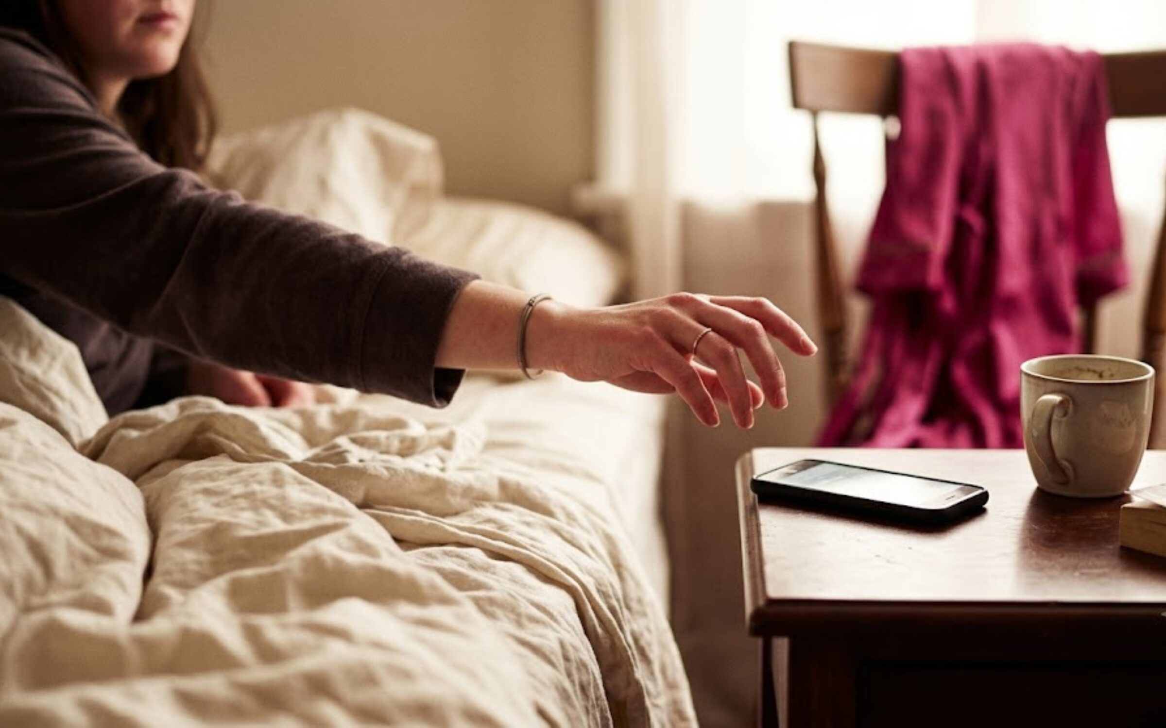 A woman's hand hesitating over a phone in warm morning light, choosing not to check in.